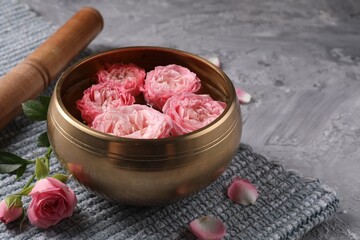 Tibetan singing bowl with water, beautiful roses and mallet on grey textured table, closeup. Space...