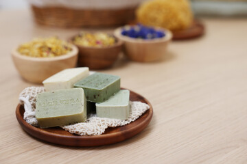 Tray with soap bars and bowls of dry flowers on light wooden table, space for text. Spa therapy