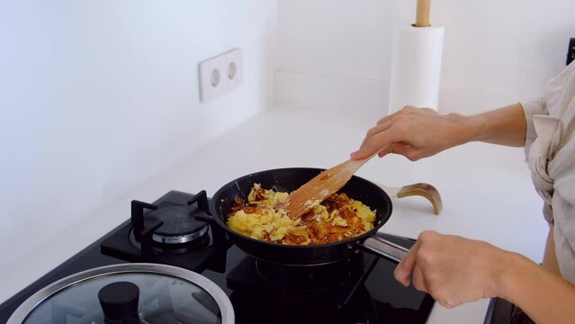 woman in kitchen make homework. woman mixes omelette with cheese and fry it in frying pan on stove. Domestic kitchen interior. Breakfast preparation.
