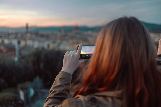 back view of female take a photo of golden sunset over Palazzo Vecchio and Cathedral of Santa Maria del Fiore (Duomo), Florence, Italy. High quality photo