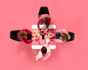 Creative collage. Aerial view of young people, colleagues eating delivery food against pink background. Copy space. Concept of business lunch, morning meeting, briefing. Ad