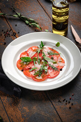 Tomato salad cut into slices with parmesan, arugula, olives and balsamic vinegar. Vegetarian Italian antipasti
