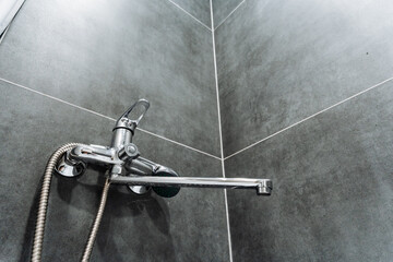 Shower faucet against grey tiled wall background in bathroom, chrome water faucet.