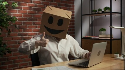 Portrait of a woman in a cardboard box with a smiling smiley face on her head. Employee at desk...