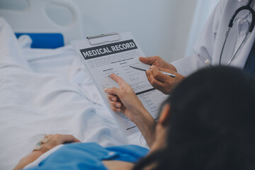 The senior woman specialist doctor with stethoscope checking up happy young Asian female patient lying in bed with receiving an intravenous saline drip in recovery room. Healthcare, medical insurance.
