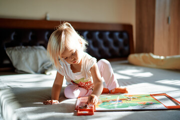 Little girl sits on the bed and collects a cardboard puzzle