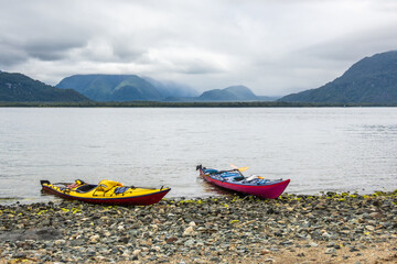 Fototapeta na wymiar sea kayaks (singler and double) on a beach in the chonos archipelago, patagonia, chile with sea and mountains in backbground room for text