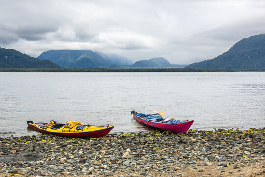 sea kayaks (singler and double) on a beach in the chonos archipelago, patagonia, chile with sea and mountains in backbground room for text