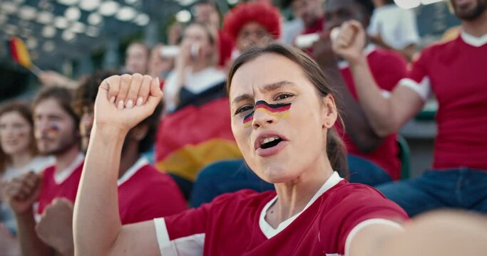 Beautiful Caucasian female holding camera and recording herself yelling something at sports event. Woman with German flag painted on her face. Having great time while supporting team.