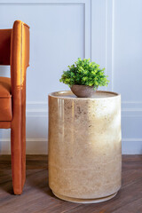 Still life of a potted plant on a coffee table beside an orange chair. The table is made of marble with beige color, and it has a round top and a pedestal base