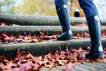 Close up of woman in rubber boots walking on footpath in autumn.