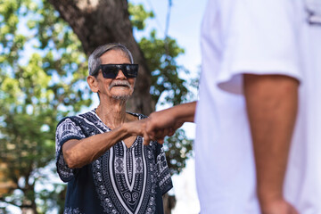 A cool hippie granddad makes a fist bump with a friend or his son. Wearing shades and boho style...