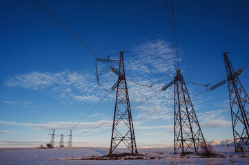 High-voltage power transmission line with towers in the field in winter at sunset in the evening