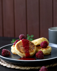 Cheese fritters Syrniki with raspberries and honey on a plate. Ukrainian cuisine food. Vertical photo