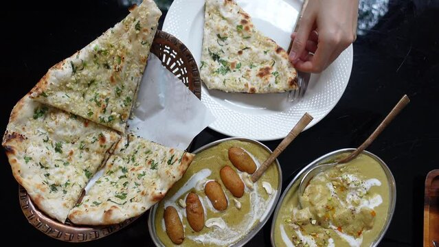 Hand using spoon scooping Indian curry top on garlic naan top view Asian Indian food