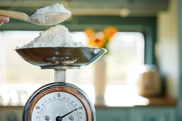 Woman's hand putting flour on an antique scale on the kitchen counter