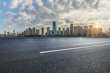 Empty asphalt road and city buildings skyline at sunset