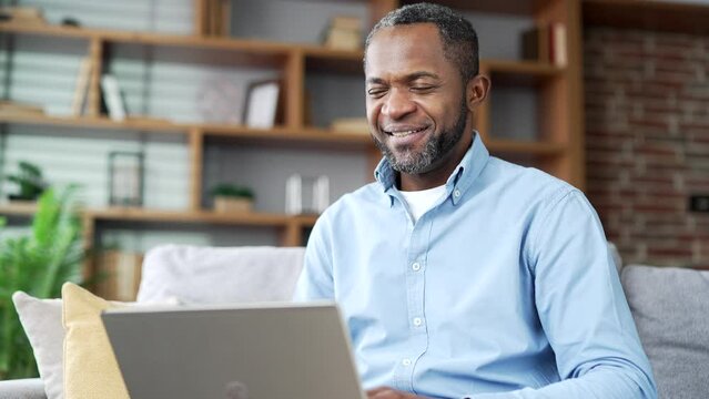 Mature african american businessman talking on video call using laptop while sitting on sofa in living room at home office. A confident entrepreneur conducts a remote meeting with business partners