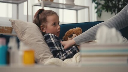 Mother taking care of sick child, little girl coughing while lying on the couch