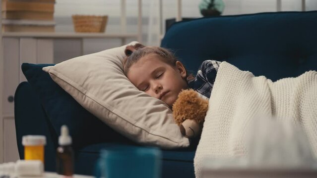 Sick little girl sleeping with a teddy bear on sofa, flue medicine on table