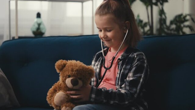 Little girl playing doctor at home, listening to her teddy bear with stethoscope