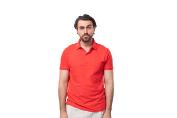 young surprised european brunette man with a beard dressed in a red t-shirt looks at the camera on a white background with copy space