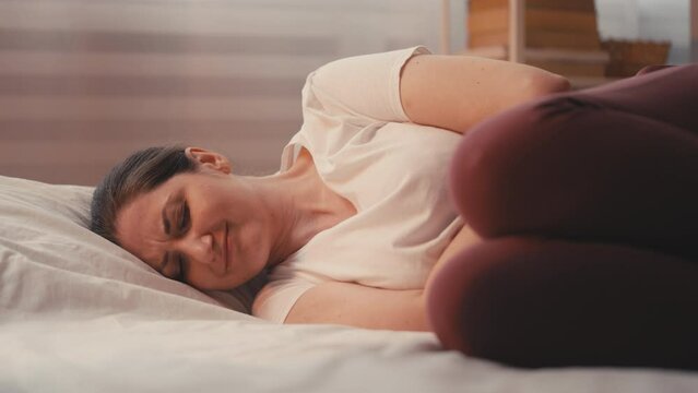 Woman in bed with abdominal pain, coping with gastritis or menstrual cramps