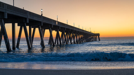 Sunrise illuminates a pier at Wrightsville Beach, casting long shadows over the ocean waves.