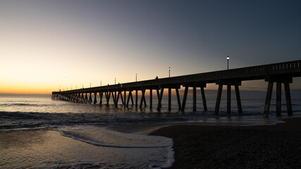 Sunrise illuminates a pier at Wrightsville Beach, casting long shadows over the ocean waves.