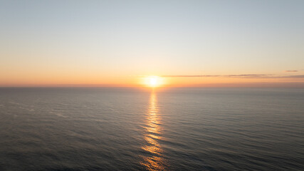 The sun sets over a calm sea, with its golden reflection stretching across the water to the horizon.