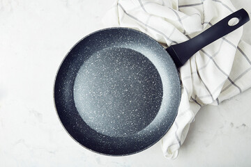 Black non-stick stainless steel frying pan on a marble background. Template. - obrazy, fototapety, plakaty
