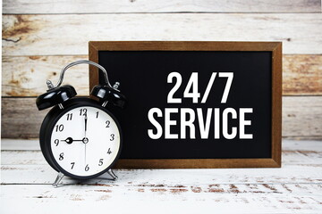 24 HRS 7 DAYS service text message and alarm clcok on wooden background