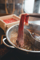 Dipping a sliced piece of pork into water hot pot during eating shabu or sukiyaki meal. Eating food action photo