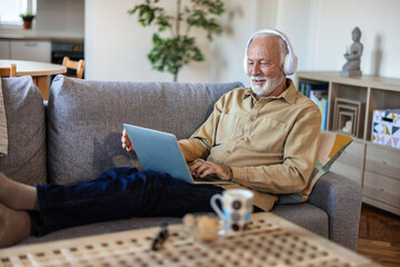 Shot of an elderly man wearing headphones and using a digital tablet on the sofa at home.