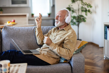 Shot of an elderly man wearing headphones and using a digital tablet on the sofa at home.