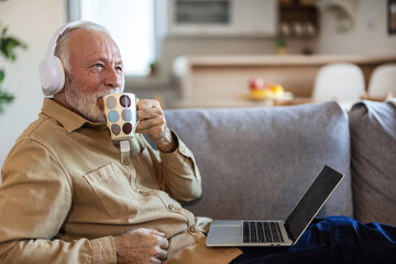 Senior man relaxing and using technology at home. Senior man with laptop and headphones at home.