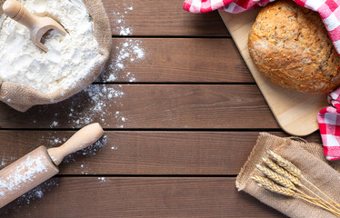 bread with flour sack, rolling pin and wheat ears on wooden background