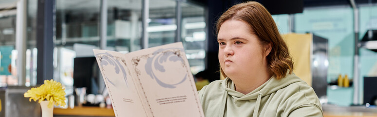young woman with down syndrome holding menu card and thinking in modern cafe, horizontal banner