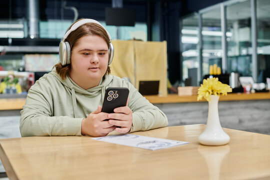 woman with down syndrome holding smartphone and listening music in headphones in cozy cafe