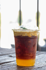 Iced fresh orange juice with espresso in a take away glass on wooden table in cozy cafe on background.