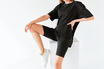 A woman wears an oversized black shirt. dark streetwear outfit young girl. Girl in stylish total black outfit mock-up. Dark t-shirt on white background.