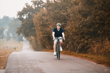 A young and fit cyclist on a bicycle explores the country landscape, riding on a road in the forest with a helmet and a mountain bike. Gravel biker on a path, enjoying the sport and the nature.