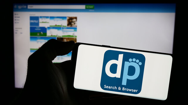 Stuttgart, Germany - 12-19-2023: Person holding mobile phone with logo of metasearch engine Dogpile in front of company web page. Focus on phone display.