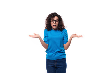 a young woman with curls dressed in a blue T-shirt shrugs her shoulders in confusion