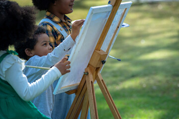 Group of African boys and girl happily paint together on canvas on an easel, amidst the bright summer atmosphere in the park, selective focus