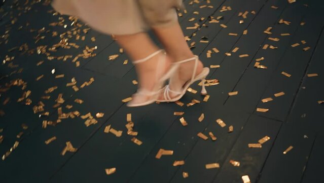 A girl is dancing merrily in shoes at an event on the floor which is strewn with festive confetti