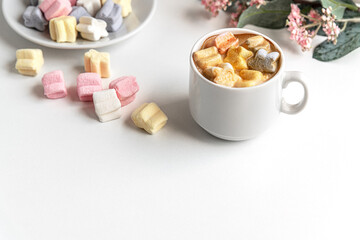cup of coffee, sweet marshmallows and pink flowers on white table