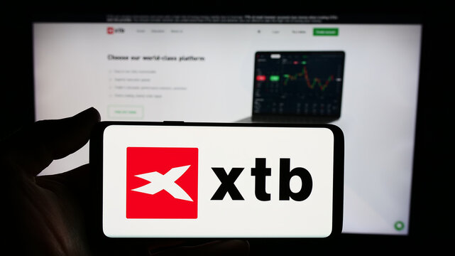 Stuttgart, Germany - 12-22-2023: Person holding smartphone with logo of Polish investment broker company XTB S.A. in front of website. Focus on phone display.