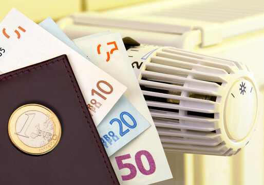 Portemonnaie mit Euroscheinen und Euromünze vor Heizkörperthermostat