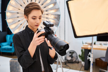 appealing concentrated woman in casual attire taking photos with her modern camera in her studio